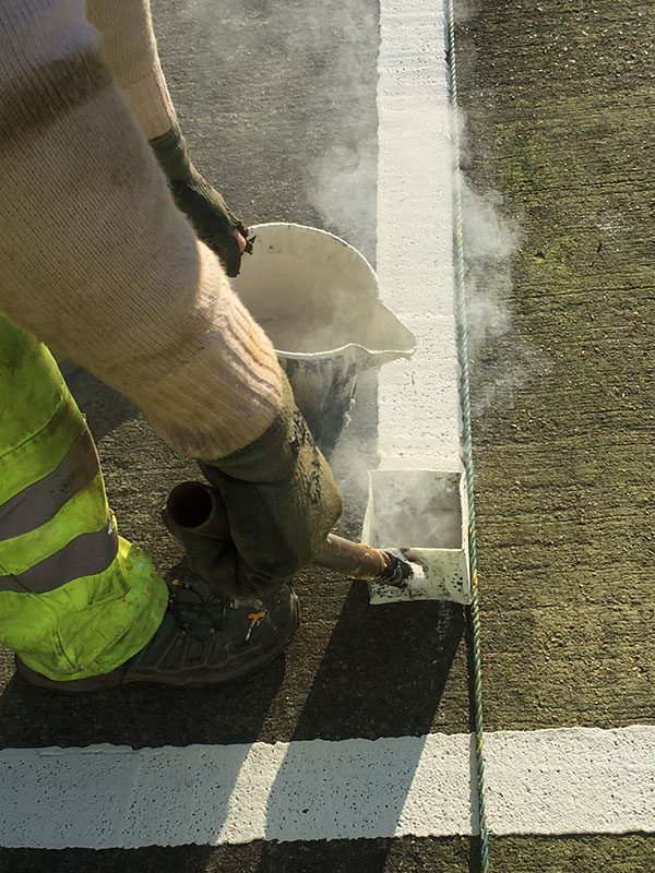 Road marking crew laying a solid white centre line on a UK road